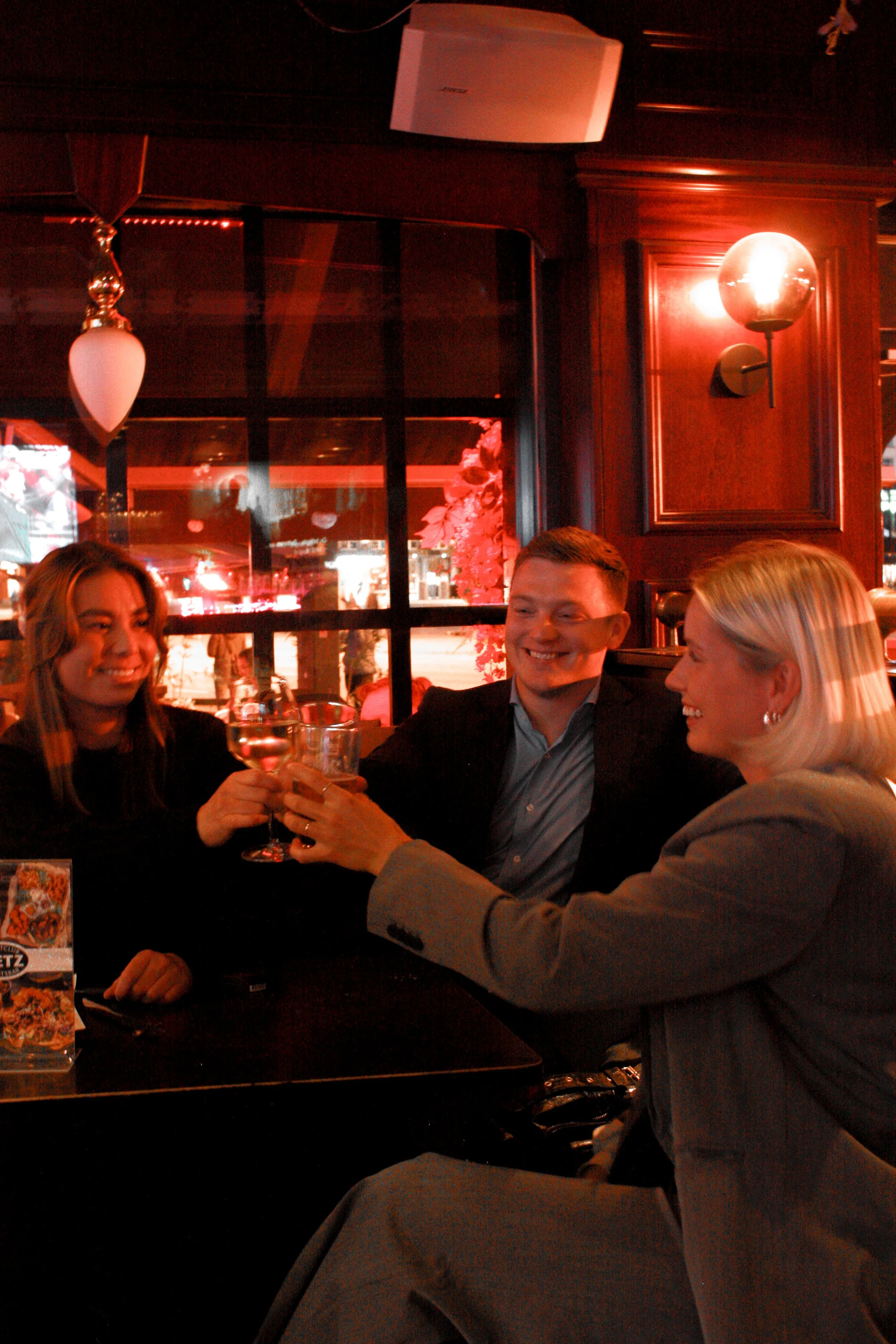 Tre venner skåler med vinglass i den rødaktige bar-belysningen hos Metz Bergen.